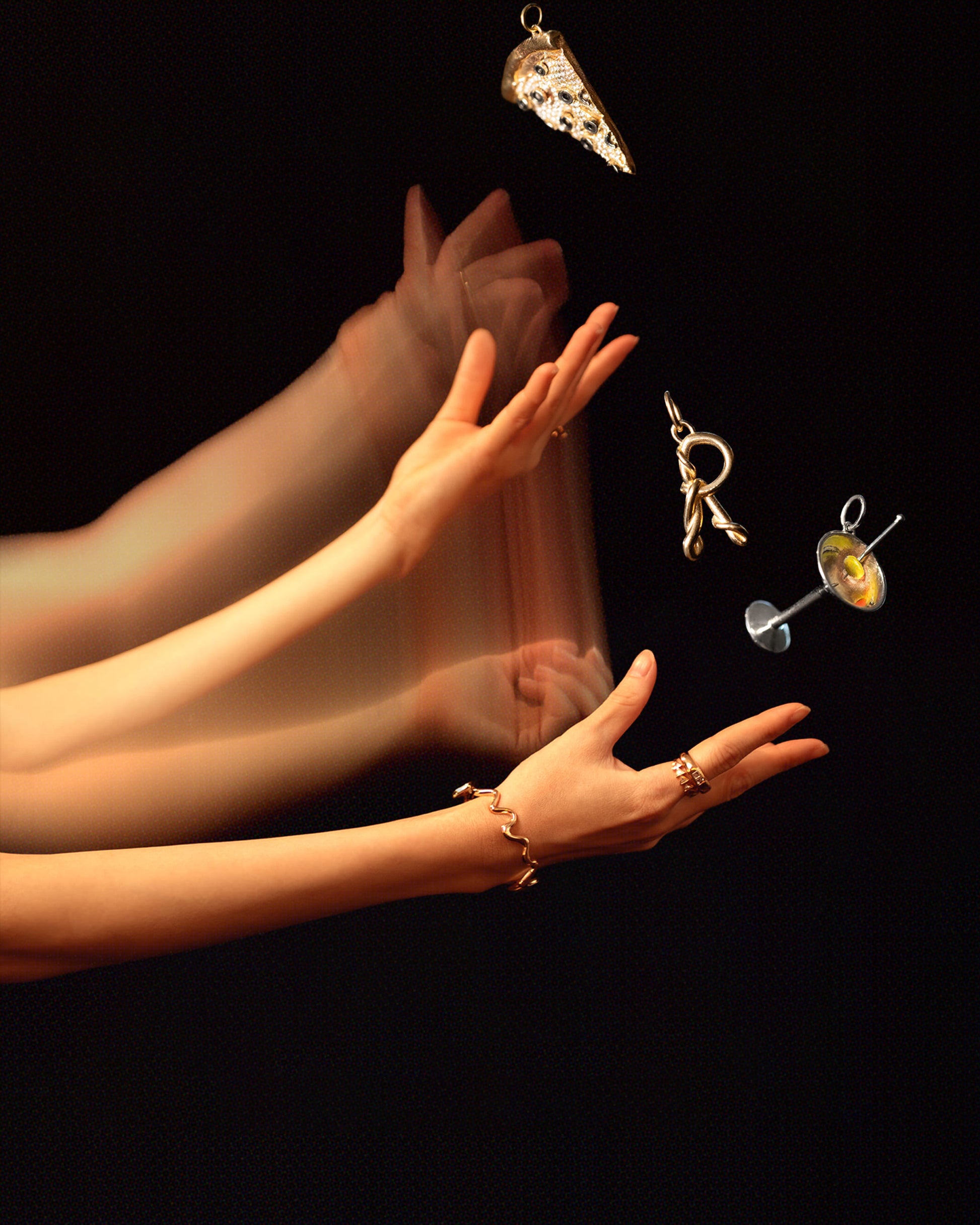 Styled long exposure image featuring the Veggie Slice Pizza Charm, Dirty Martini Charm, Gold Cut-Outs Bracelet and CRZM by Mociun Gold R Letter Charm on dark color background.