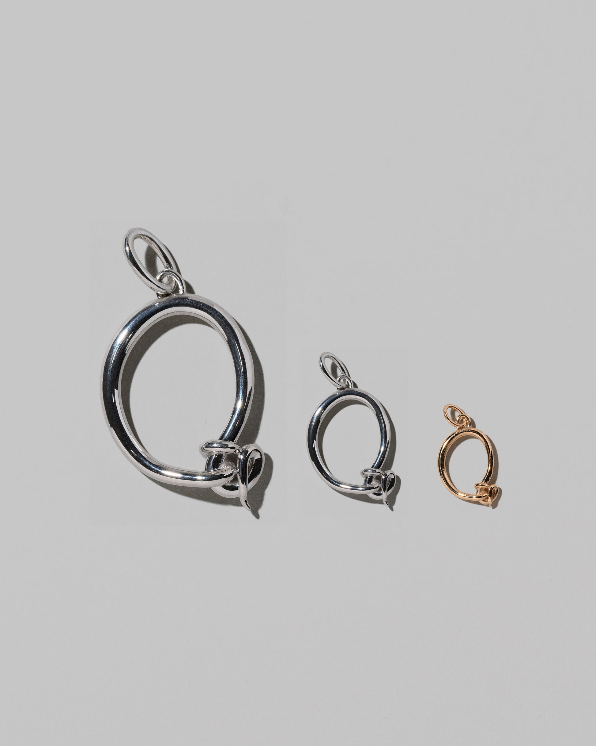 CRZM Large Sterling Silver, Medium Sterling Silver & Mini Letter Q Charms set in solid gold on light color background.