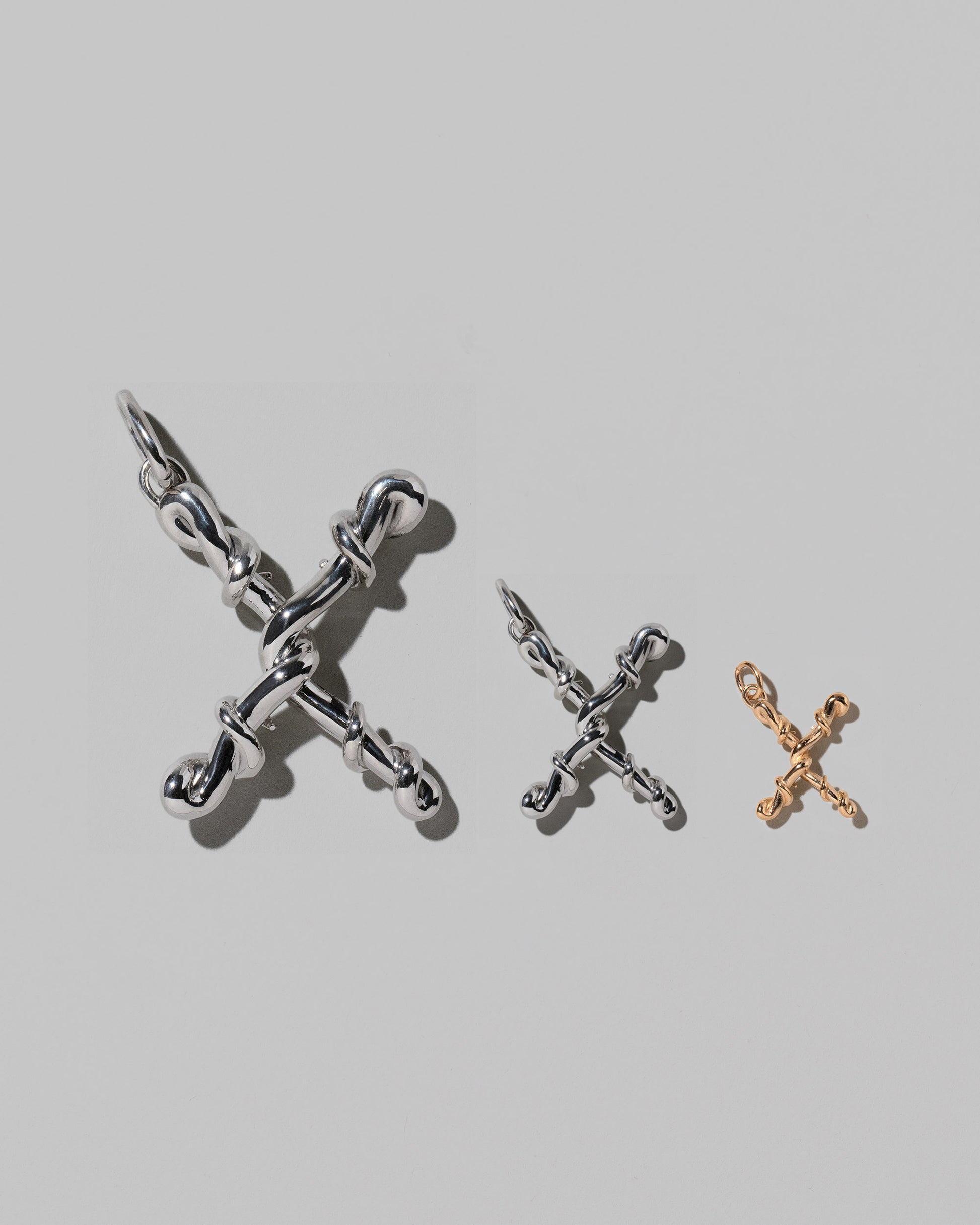 CRZM Large Sterling Silver, Medium Sterling Silver & Mini Letter X Charms set in solid gold on light color background.