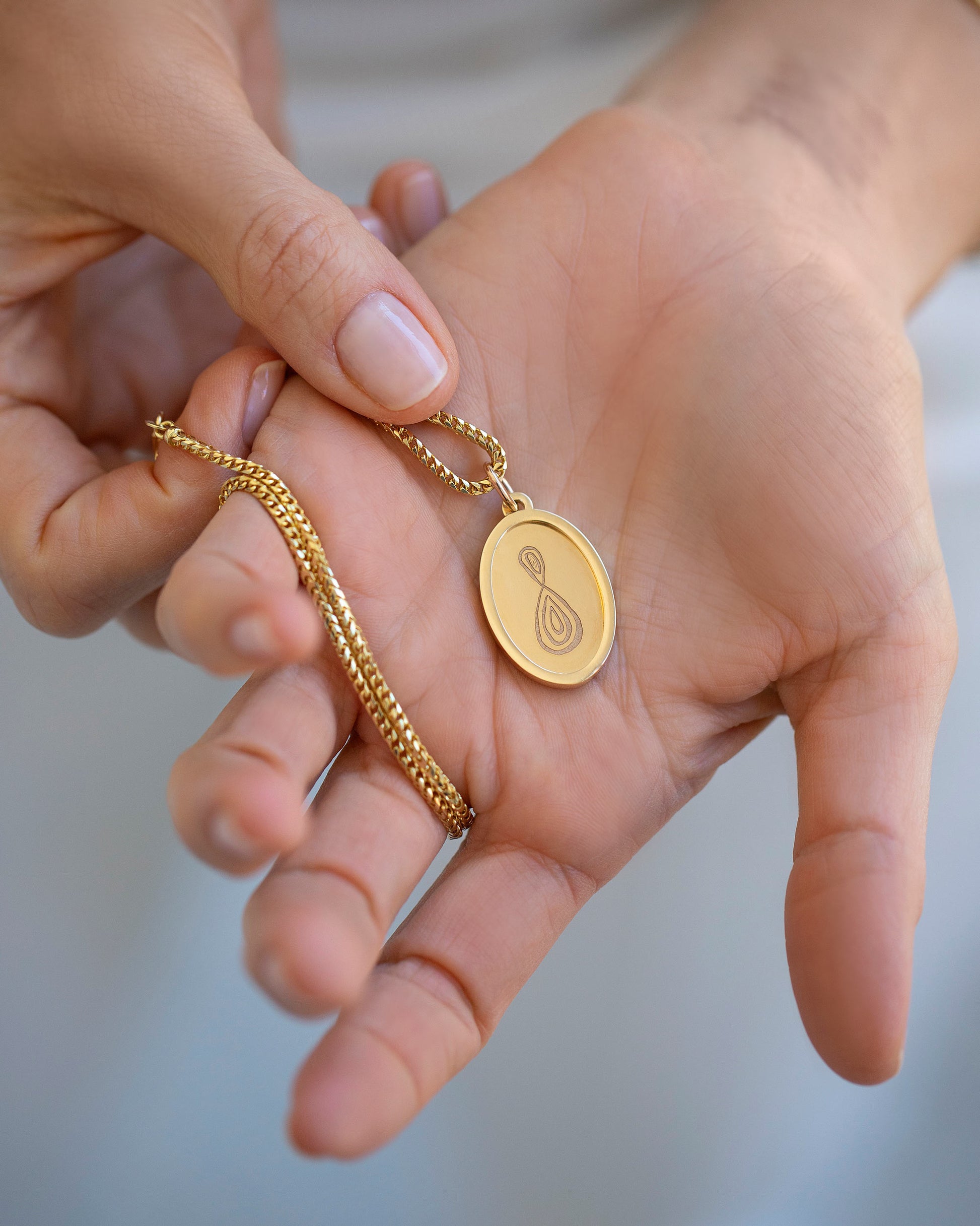 Finished Large Oval Memento Pendant engraved with an abstract symbol in hand, paired with the Mociun 2mm 18" Ritual Chain Necklace.