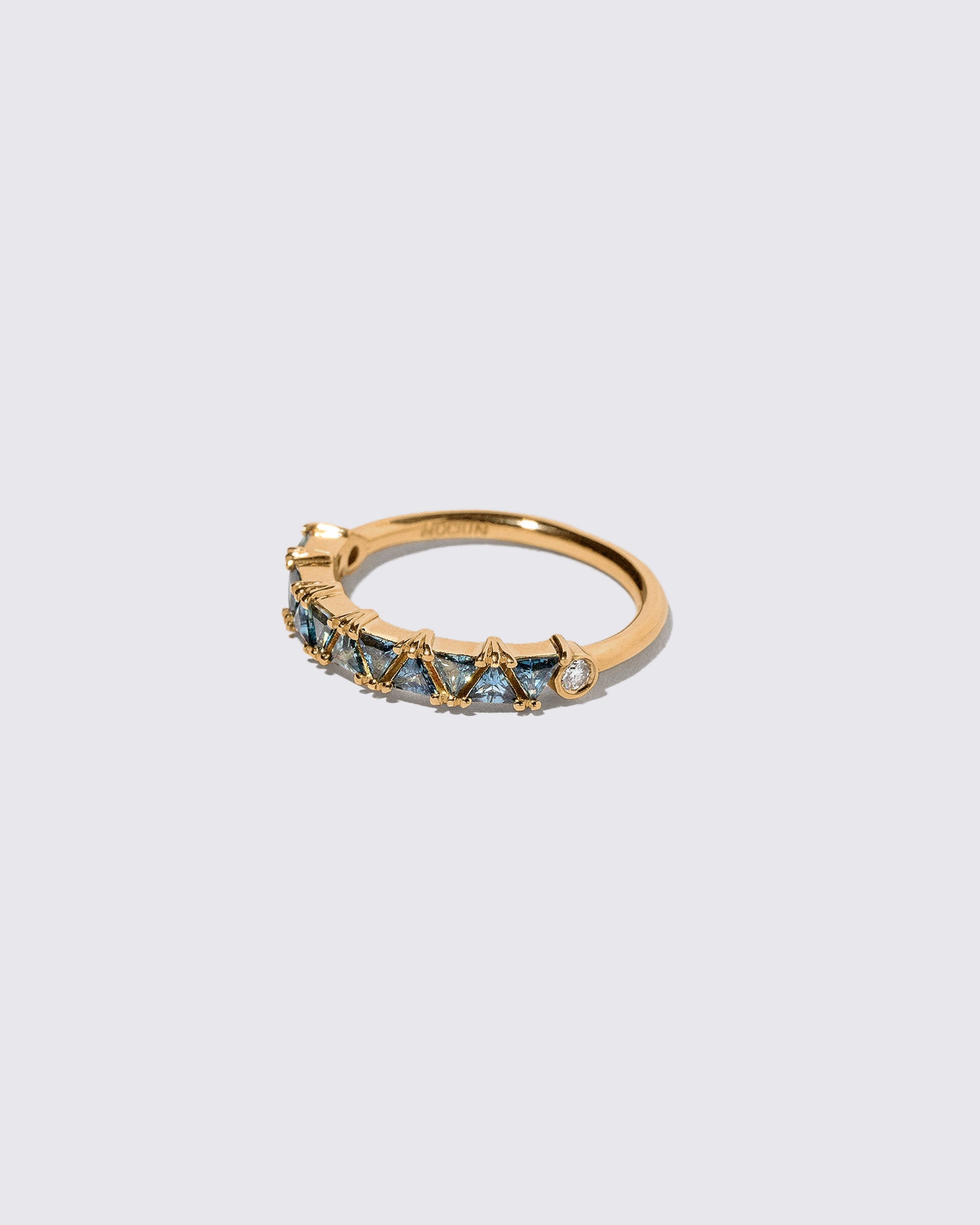 View from the side of the Teal Sapphire Eleven Trillion Ring on light color background.