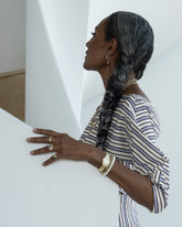 Styled image on model featuring the Blue Sapphire Gusher Charm Huggie Hoop Earrings, a Double Drop Ring the Gold 5mm Ripple Band on hand, a Link Bracelet and Gold Pearl Openable Link Bracelet on wrist and the Infinity Openable Link Necklace, Link Necklace and Petite Link Necklace layered on neck.