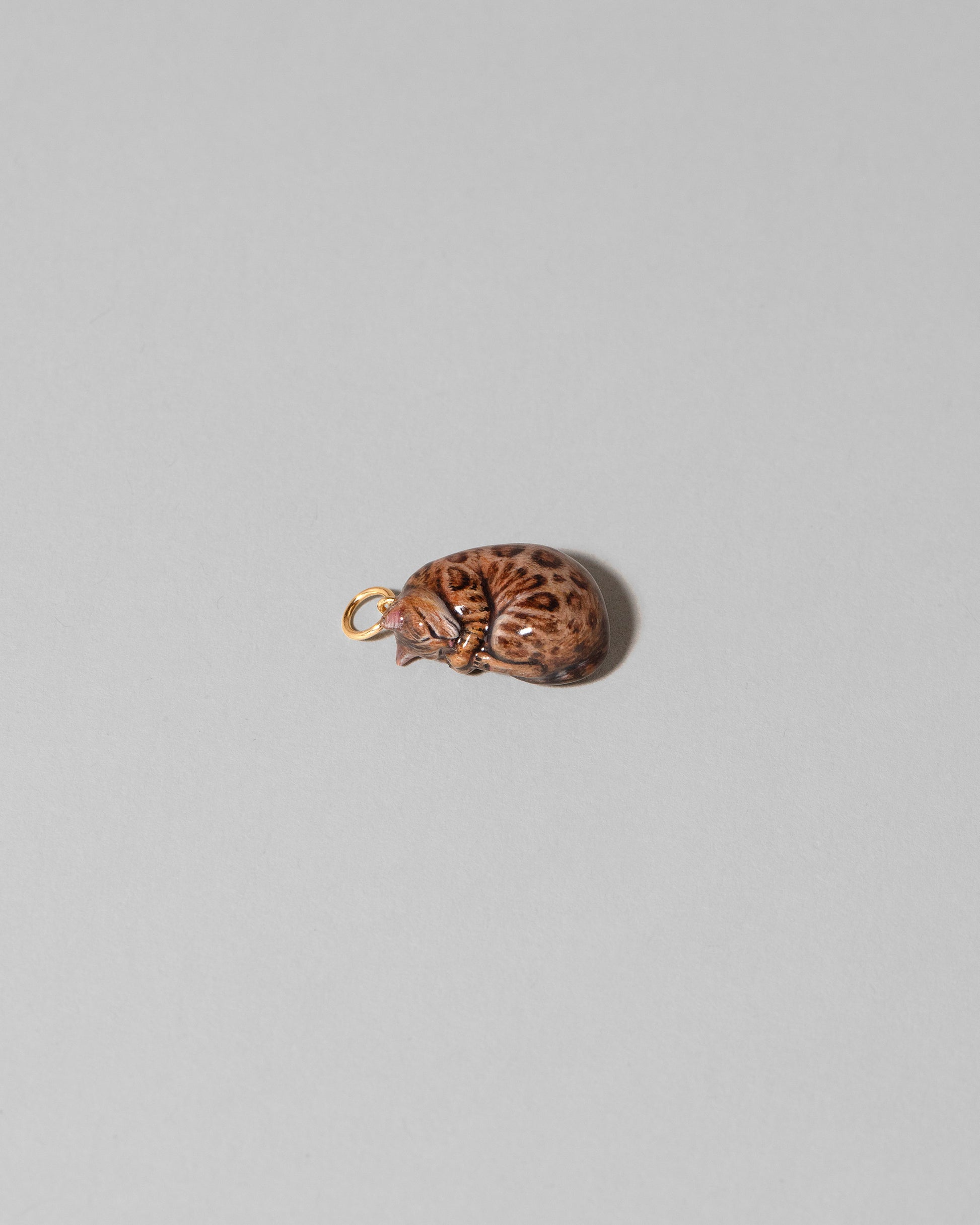 View from the side of the Bengal Curled-Up Cat Charm on light color background.