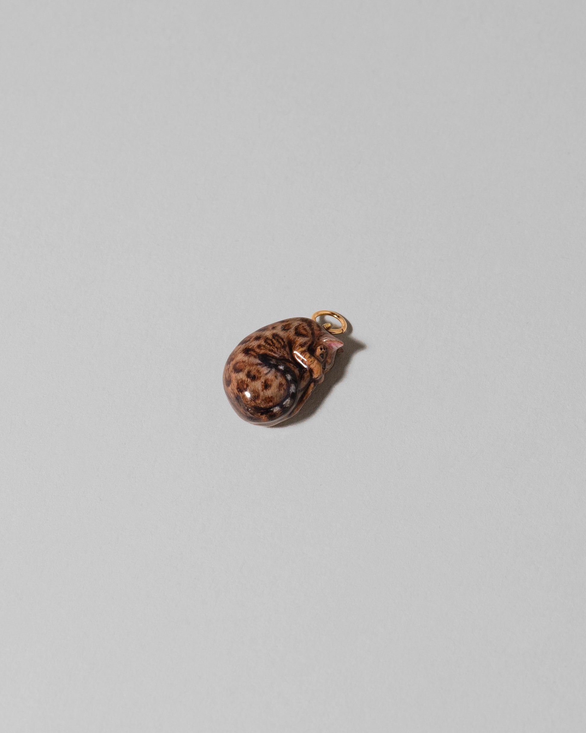 View from the side of the Bengal Curled-Up Cat Charm on light color background.