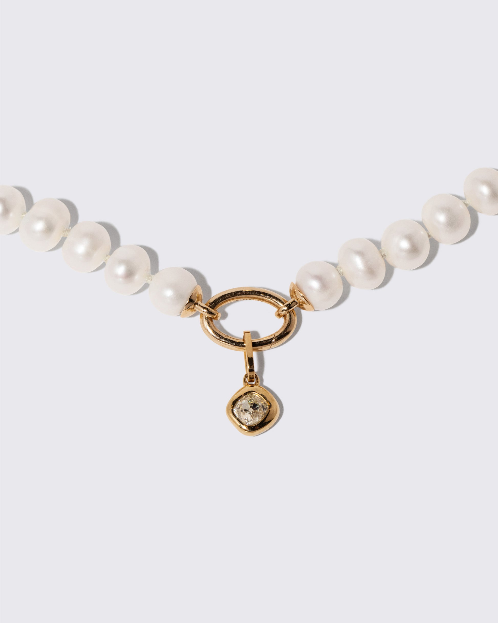 Closeup details of the Diamond Poise Charm and Gold Pearl Openable Link Necklace on light color background.