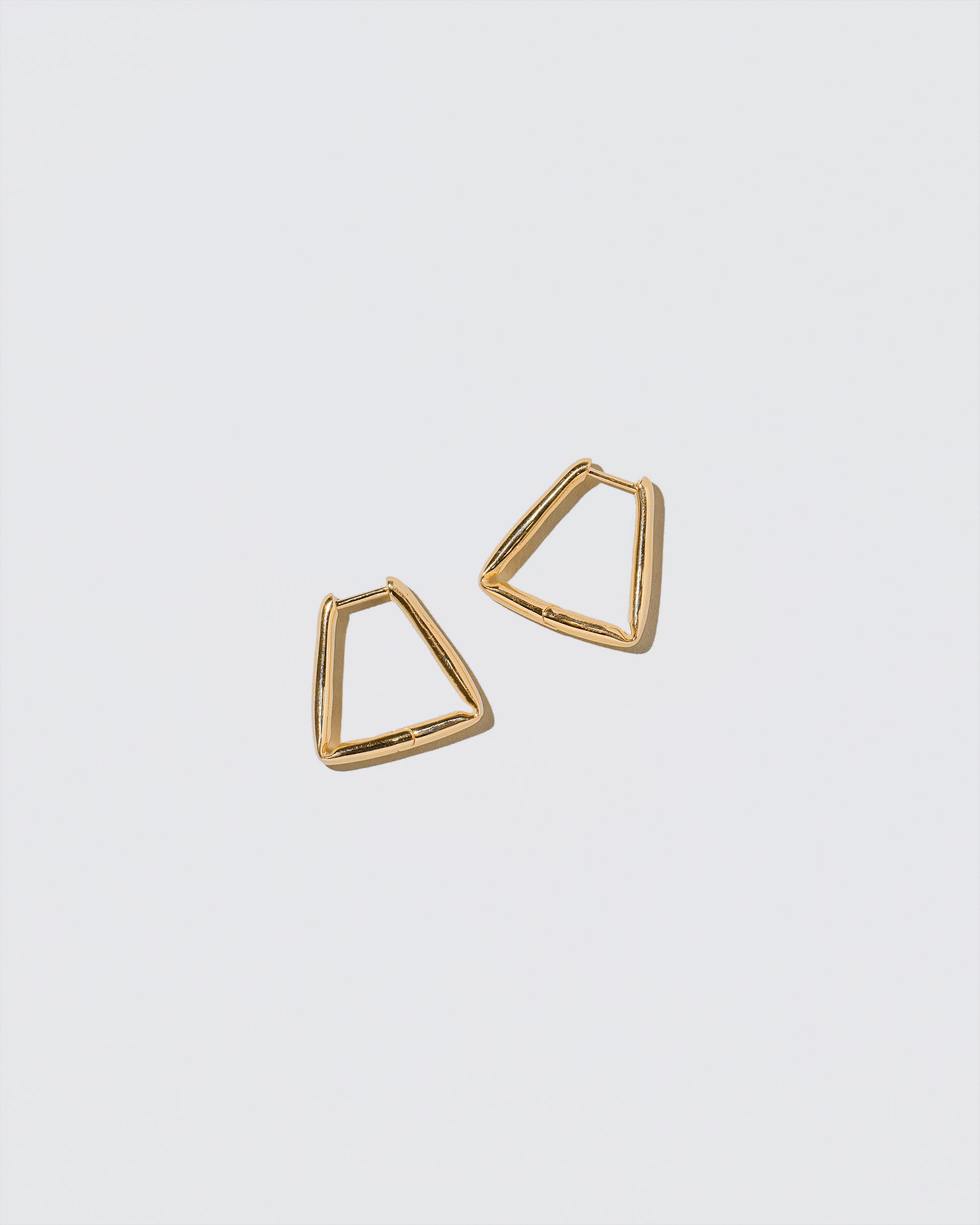 Gold Bend Hoop Earrings on light color background.
