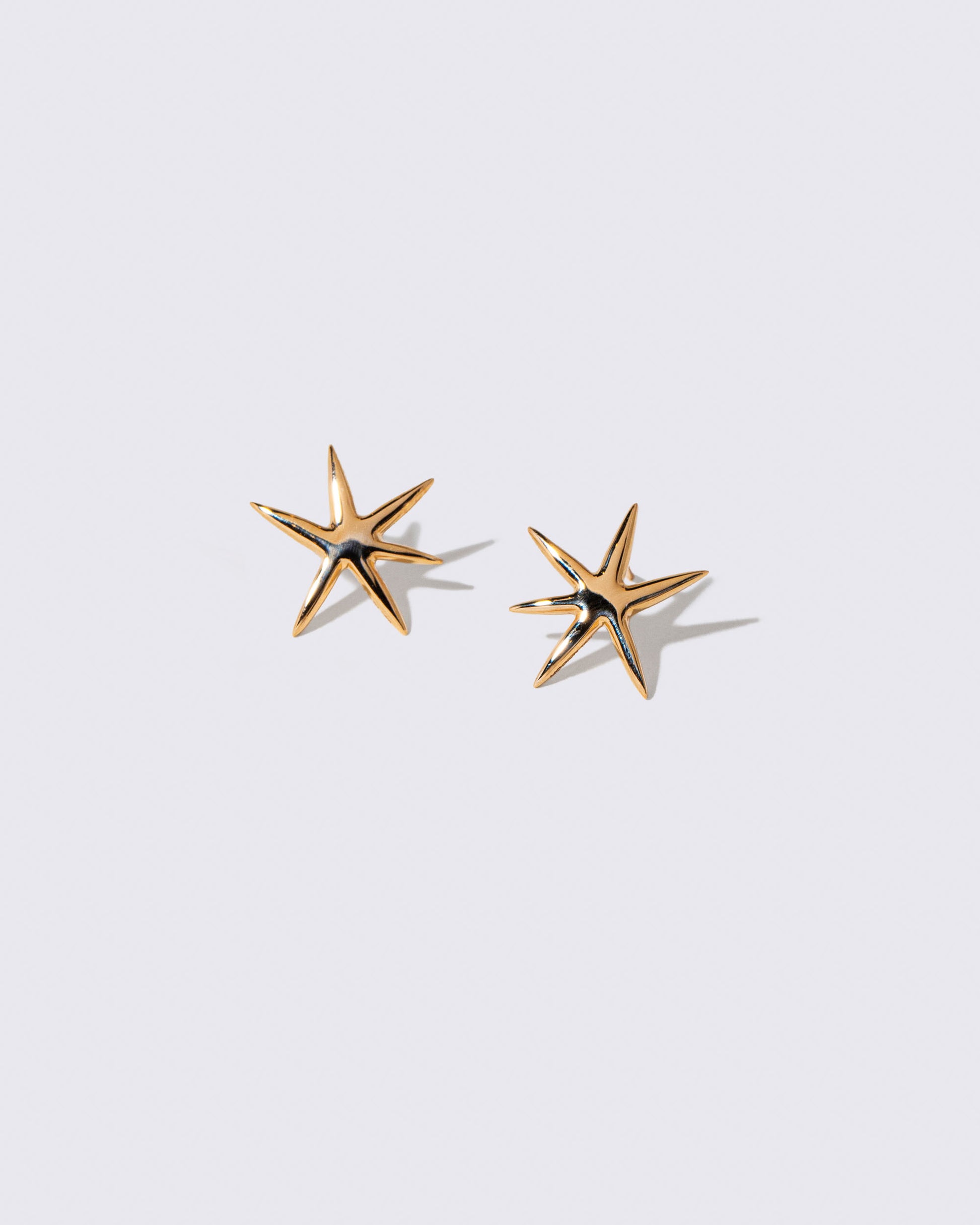 Gold Large Verve Six Point Star Stud Earrings on light color background.