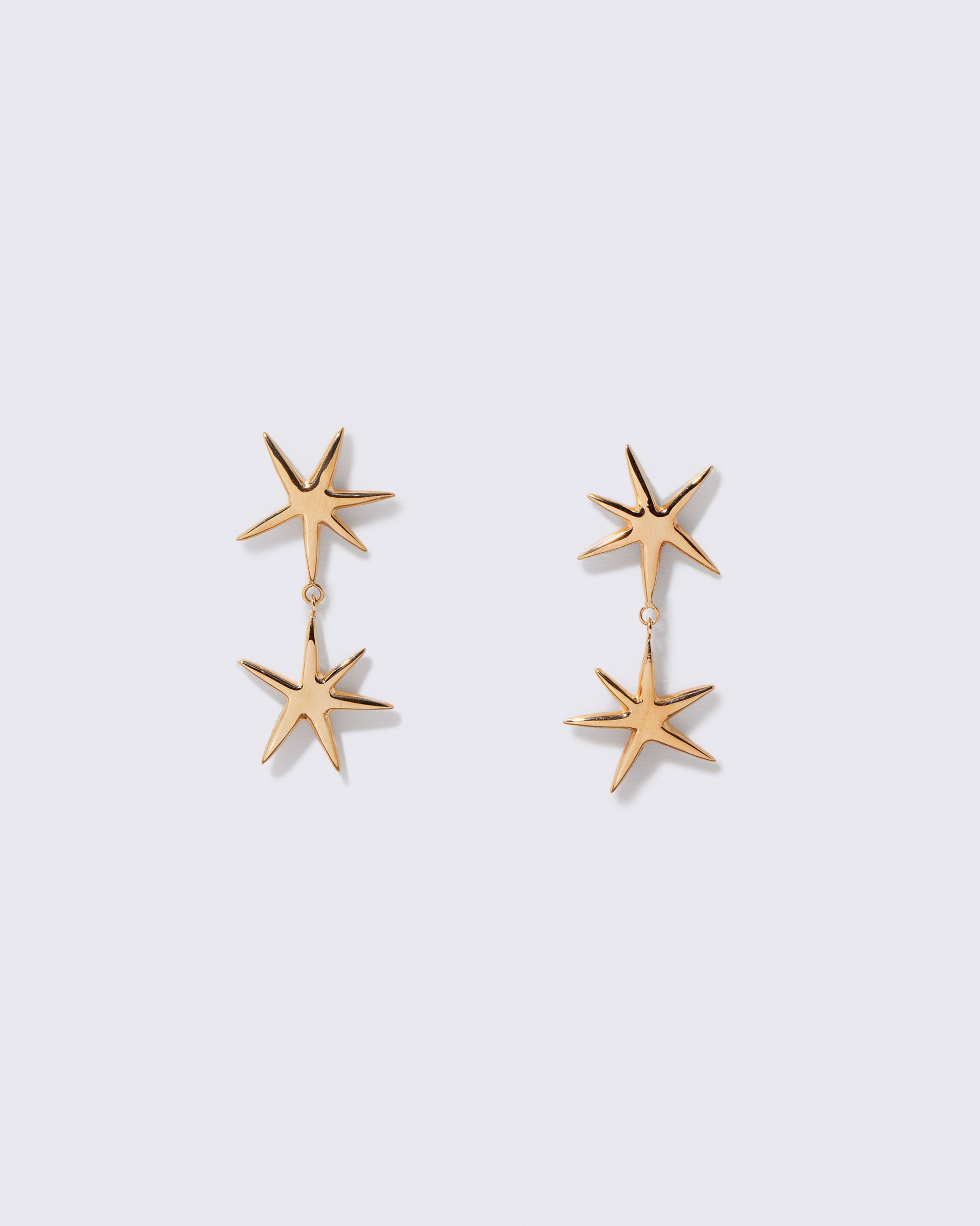 Gold Verve Star Drop Earrings on light color background.