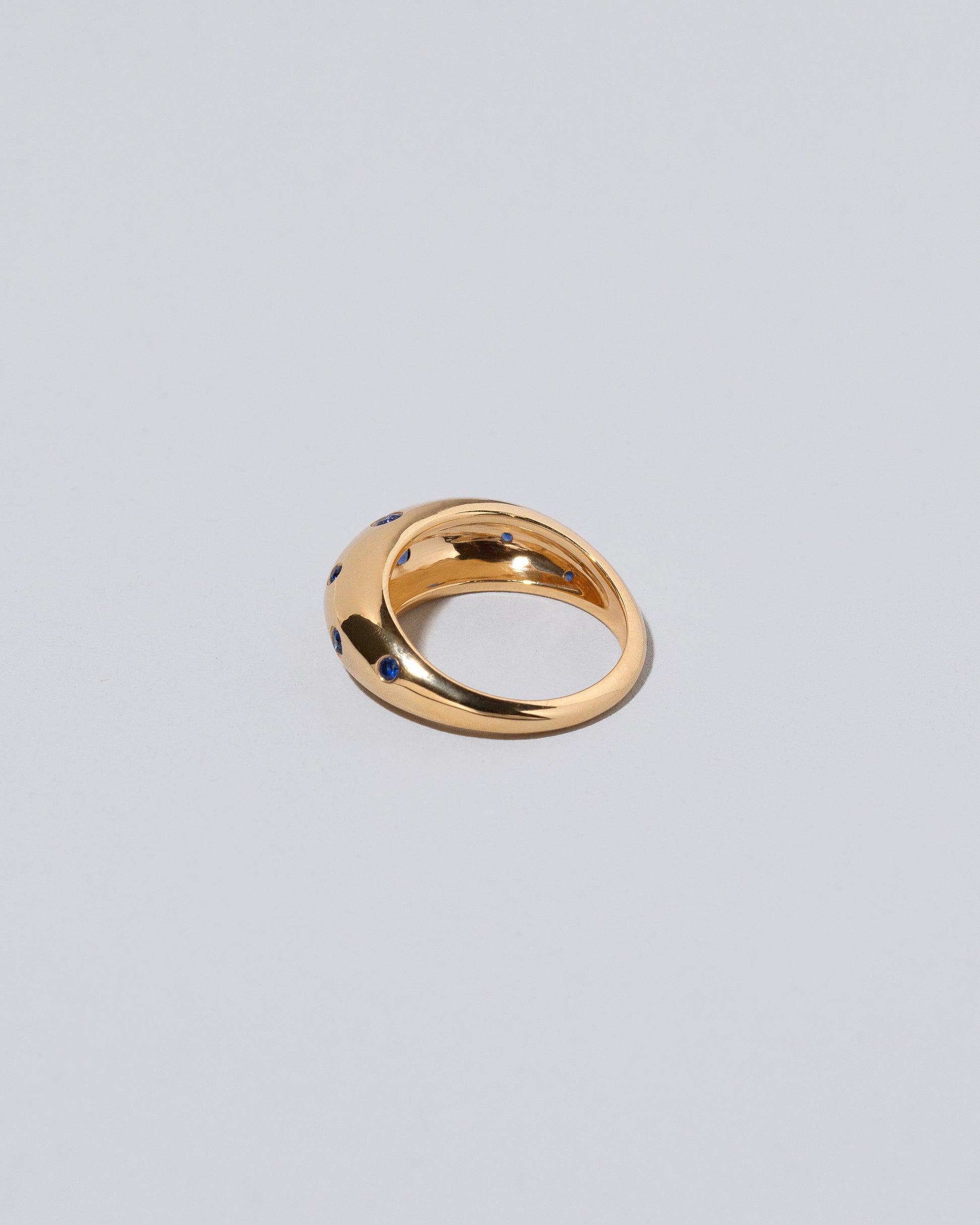 View from the back of the Gold Blue Sapphire Brilliant Cuts Light Cutter Band on light color background.