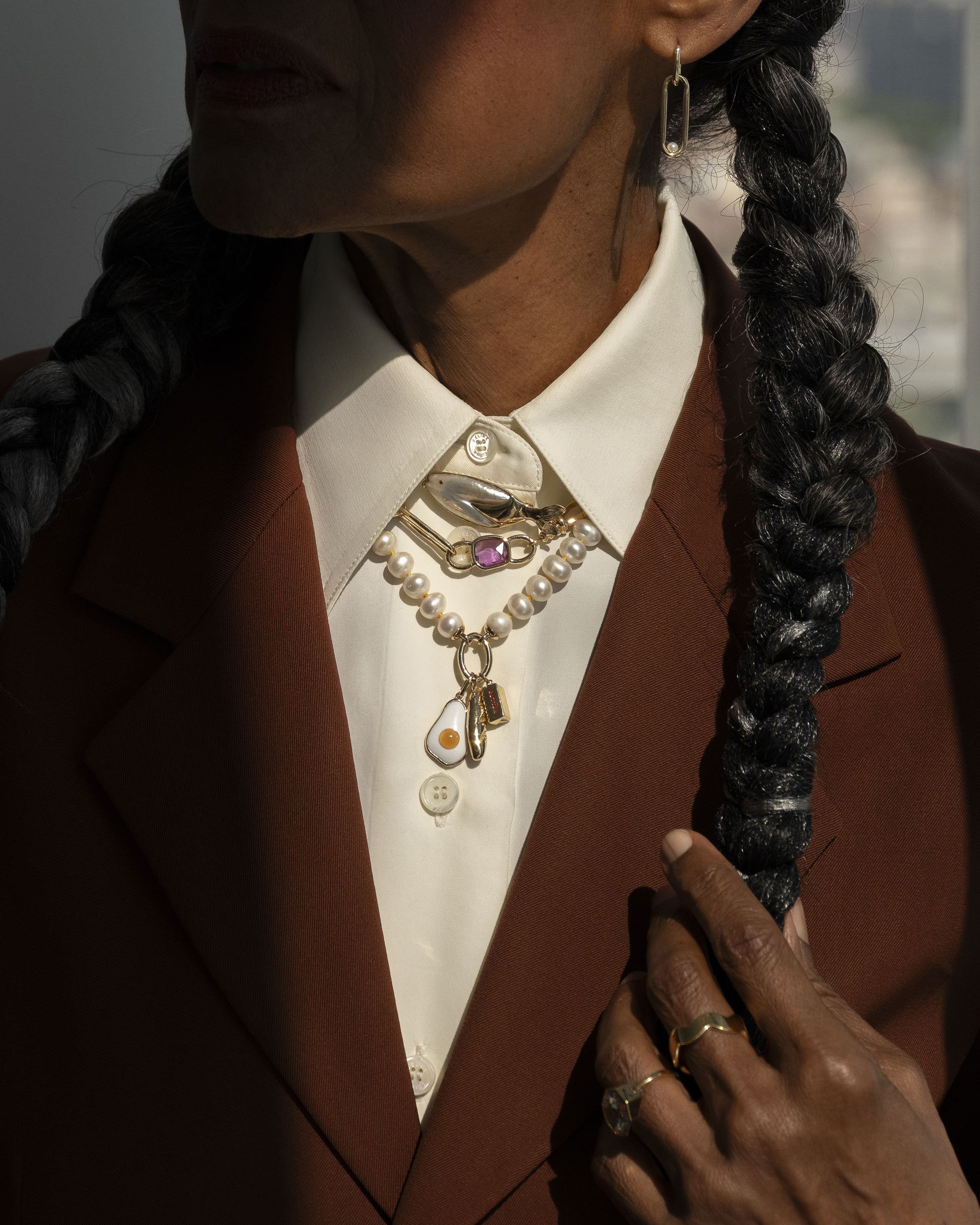 Styled image on model featuring the Gold 5mm Ripple Band, Pearl Link Huggie Hoop Earrings, the Frank Fish Brooch pinned on the collar above the Sapphire Gusher Openable Pendant on Link Necklace, and on clasp of the Gold Pearl Openable Link Necklace is a Demi Baguette Charm, Stick of Salted Butter Charm and Fried Egg Pendant.