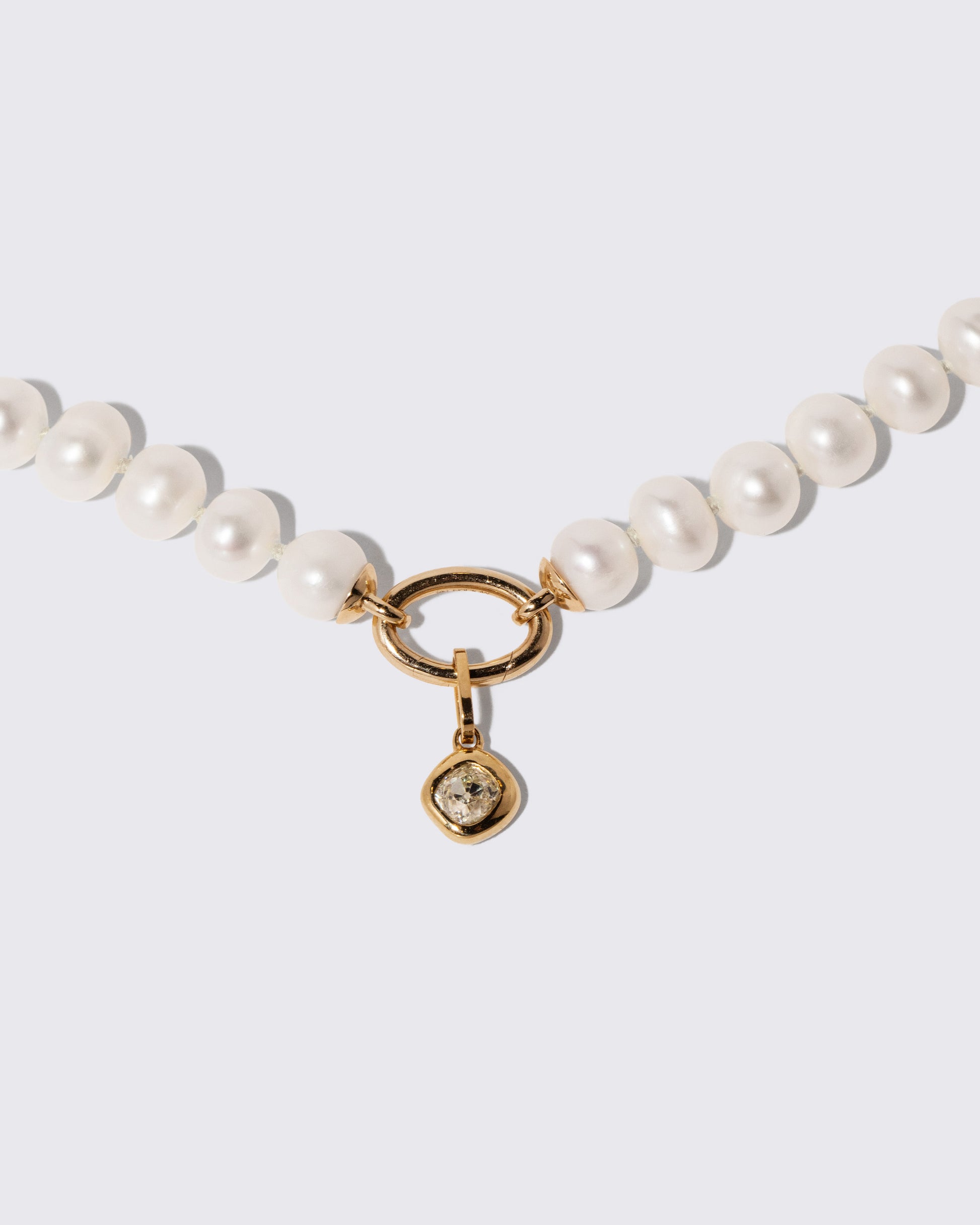 Closeup details of the Gold Pearl Openable Link Necklace and Diamond Poise Charm on light color background.