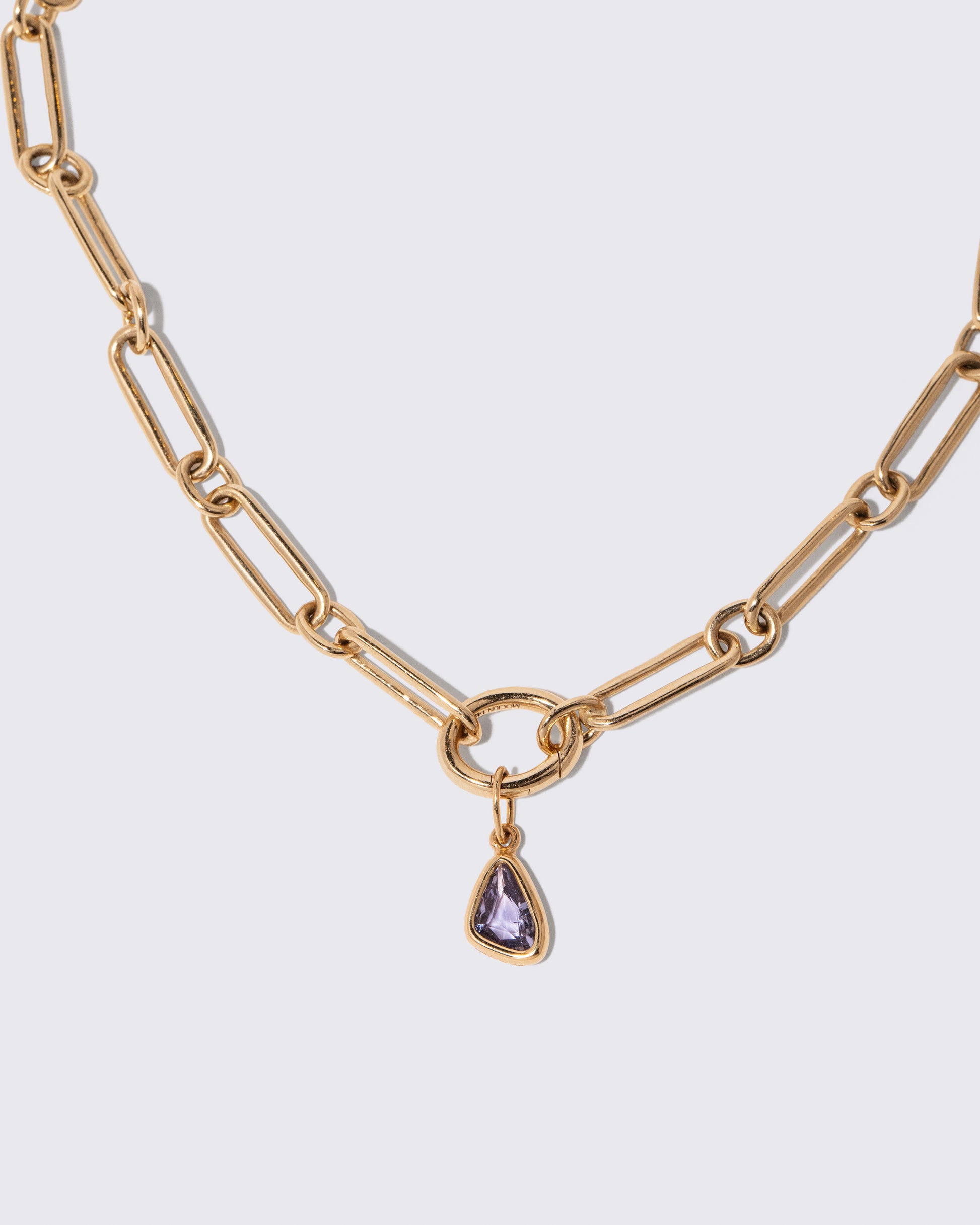 Closeup details of the Blue Sapphire Gusher Charm and Petite Link Necklace on light color background.
