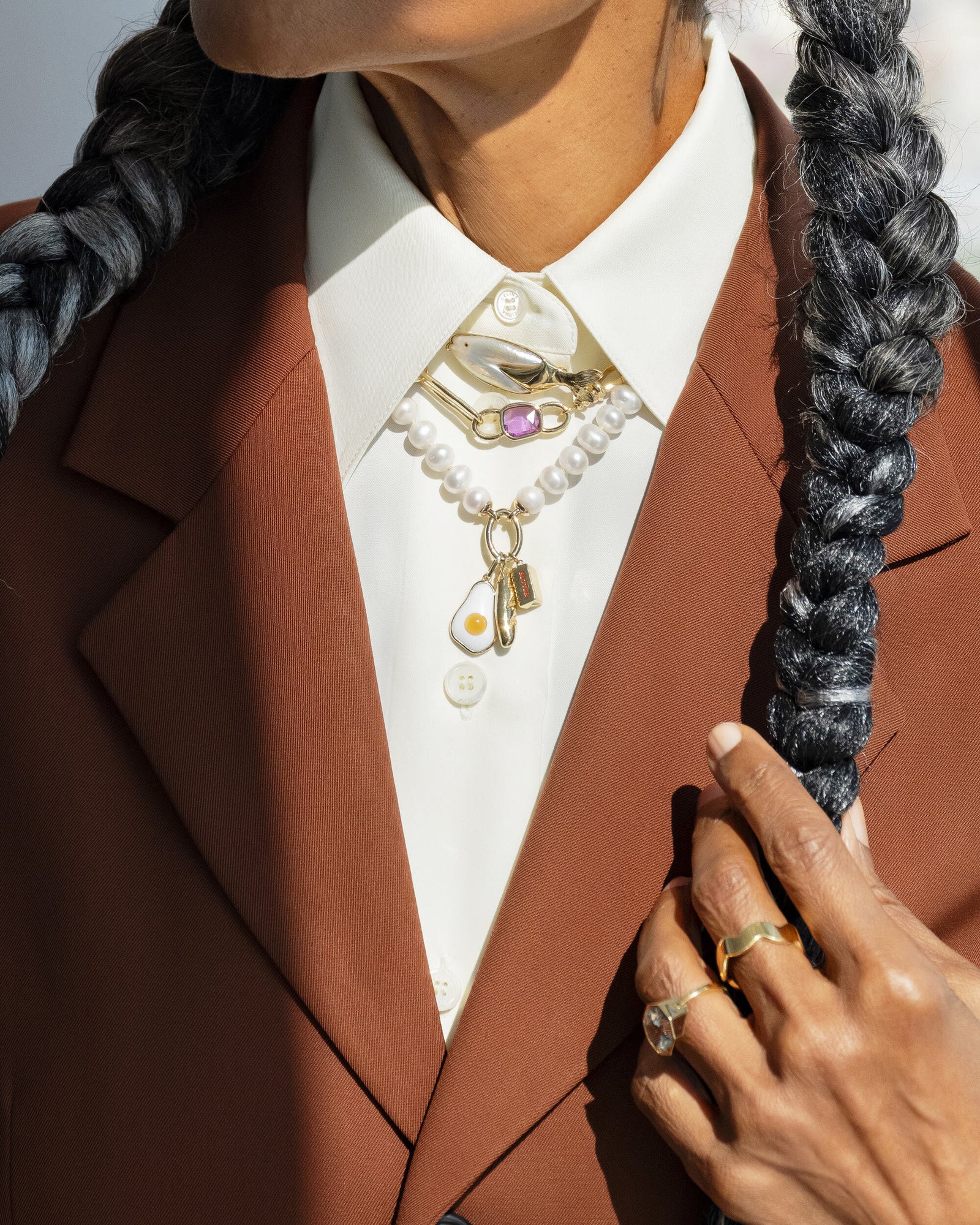 Styled image on model featuring the Gold 5mm Ripple Band, Pearl Link Huggie Hoop Earrings, the Frank Fish Brooch pinned on the collar above the Sapphire Gusher Openable Pendant on Link Necklace, and on clasp of the Gold Pearl Openable Link Necklace is a Demi Baguette Charm, Stick of Salted Butter Charm and Fried Egg Pendant.