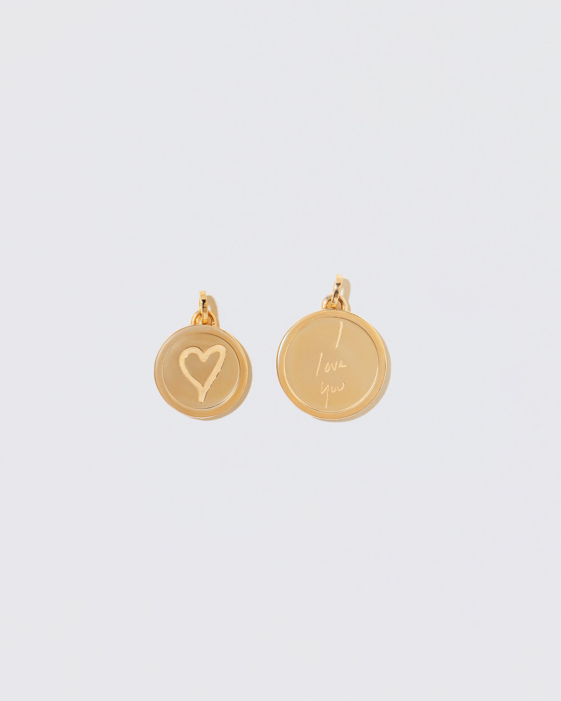 Finished Small Round Pendant Memento Pendant engraved with a heart shape and a finished Large Round Pendant Memento Pendant engraved with 'I Love You' on light color background.
