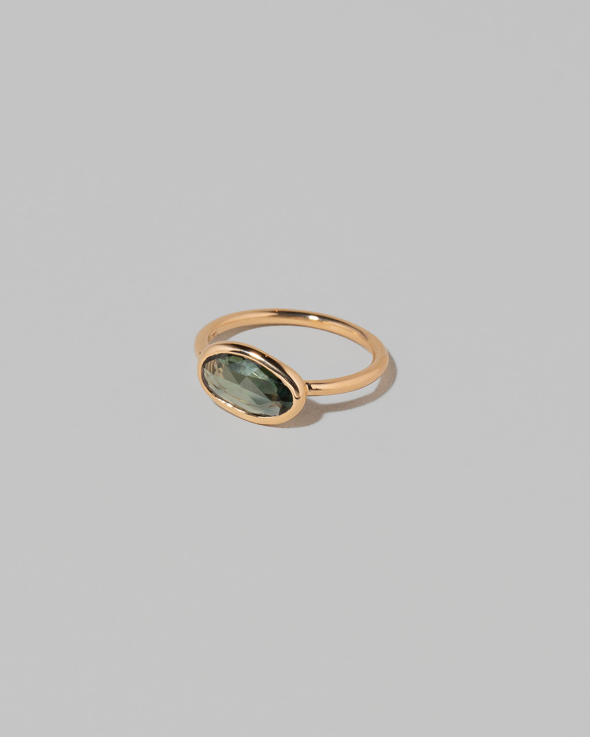View from the side of the Gusher Green Sapphire Ring 002 on light color background.