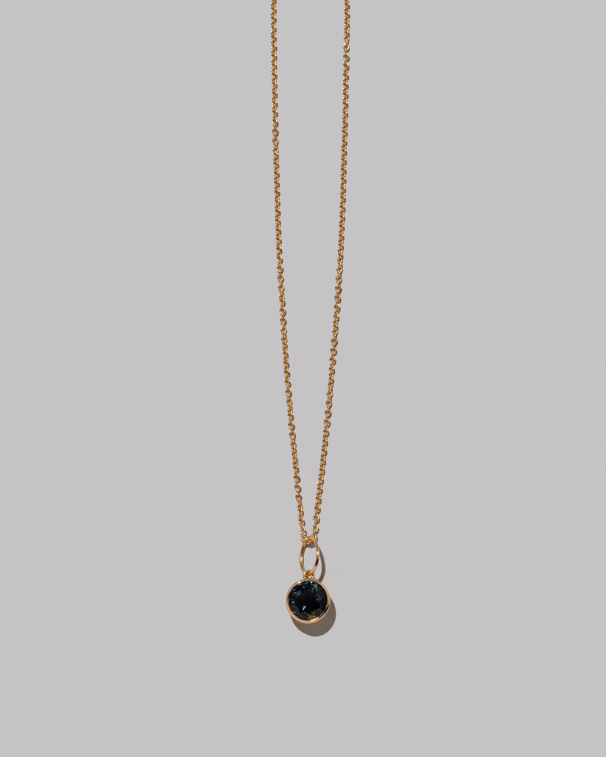 Closeup details of the Bicolor Sapphire Pendant paired with chain on light color background.