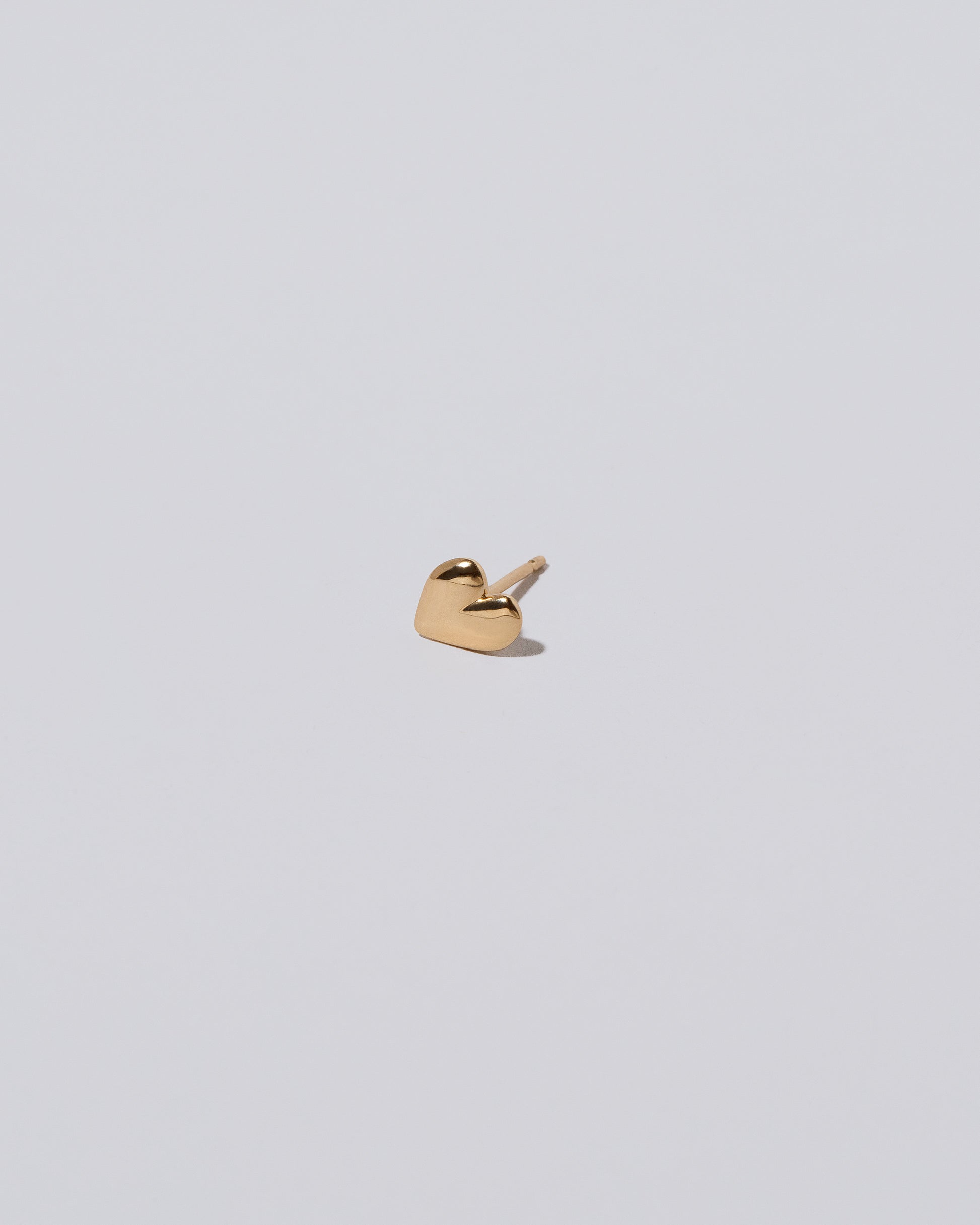 View from the side of the Shape One Small Thousand & One Night Heart Stud Earring single on light color background.