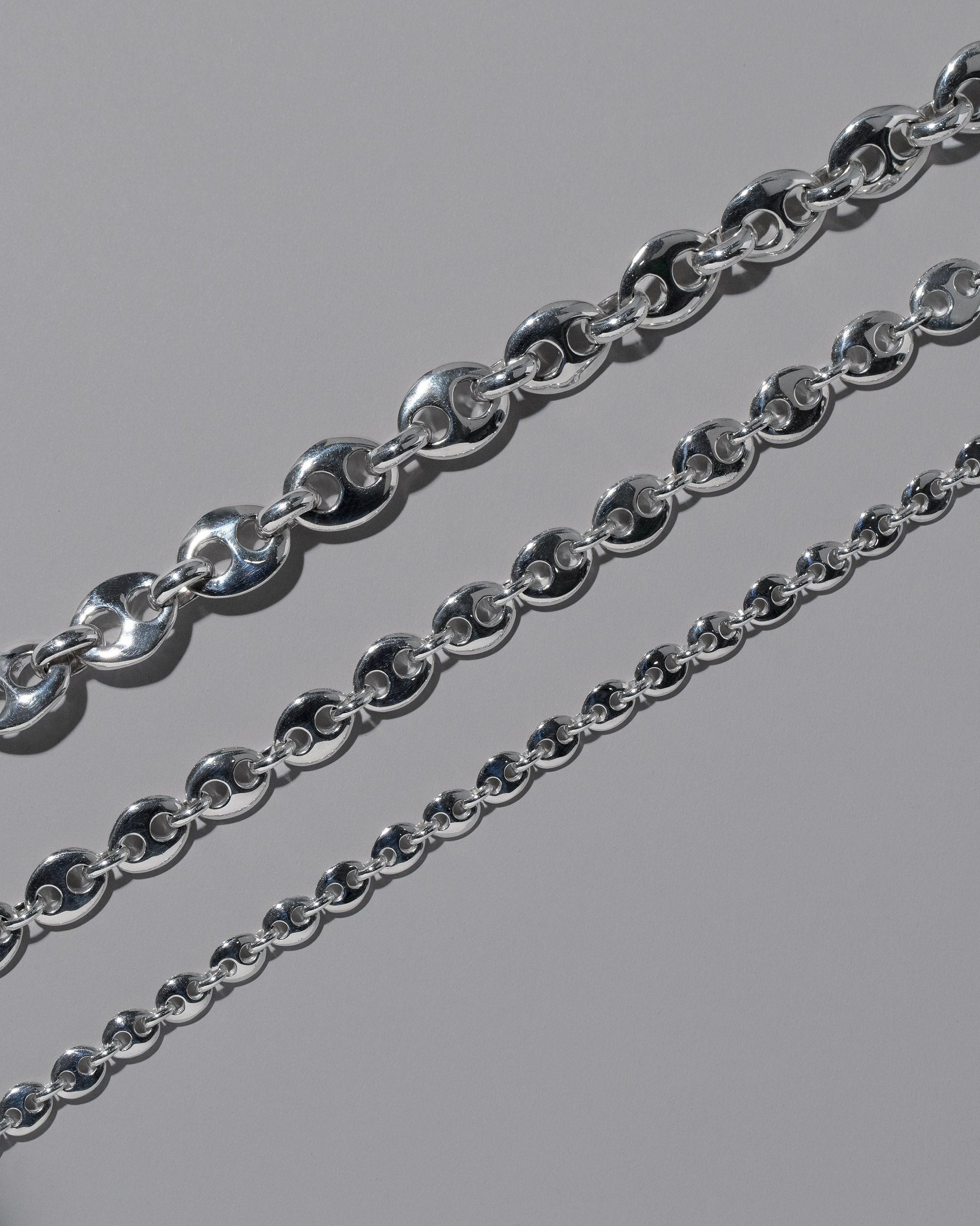 Closeup details of the CRZM Sterling Silver Bedrock Mini Necklace, Sterling Silver Bedrock Medium Necklace, and Sterling Silver Bedrock Necklace on light color background.
