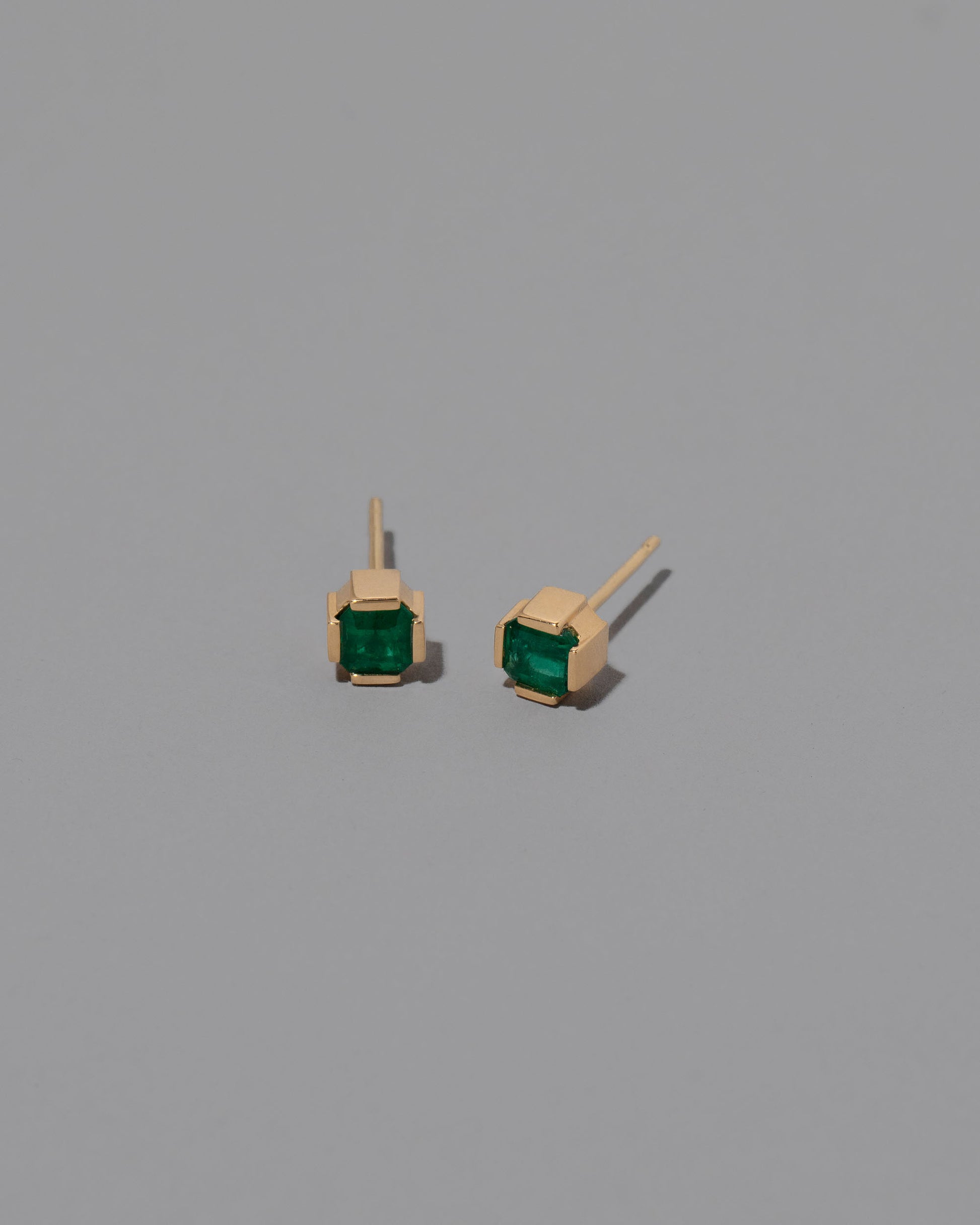 Gold Emerald Fold Earrings on light color background.