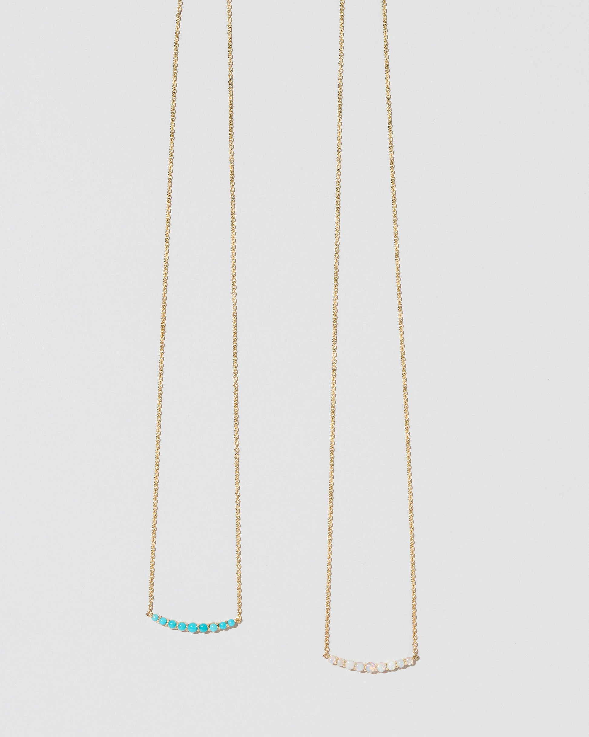 Closeup detail of the Opal Crescent Necklace and Turquoise Crescent Necklace on light color background.