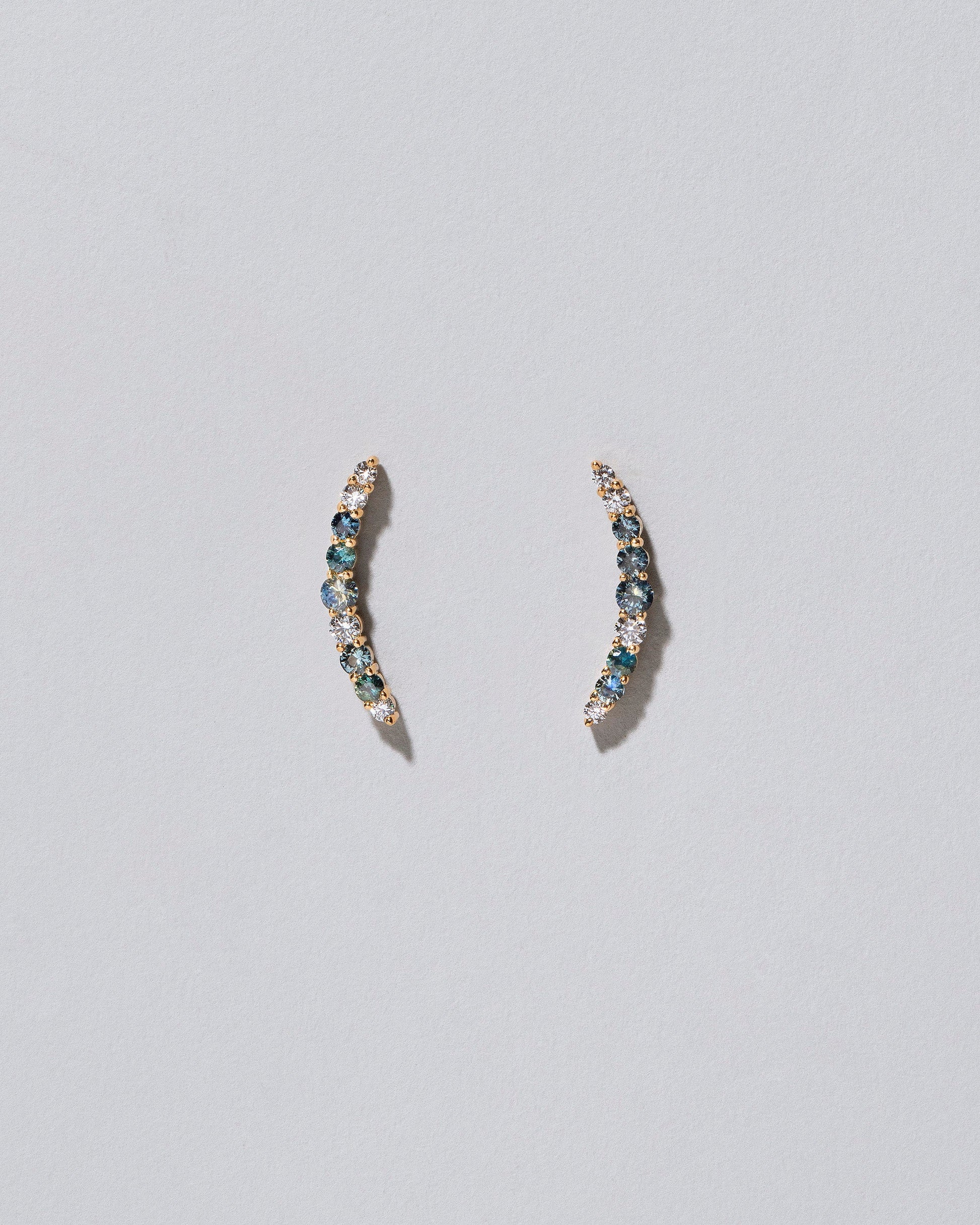 An edition of the Sapphire & White Diamond Crescent Ear Climber Stud Earrings on light colored background.