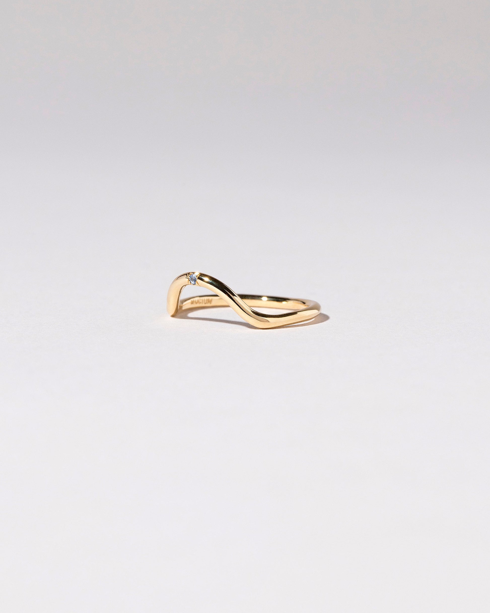 View from the side of the Gold Single Stone Blue Sapphire Curve Band on light color background.