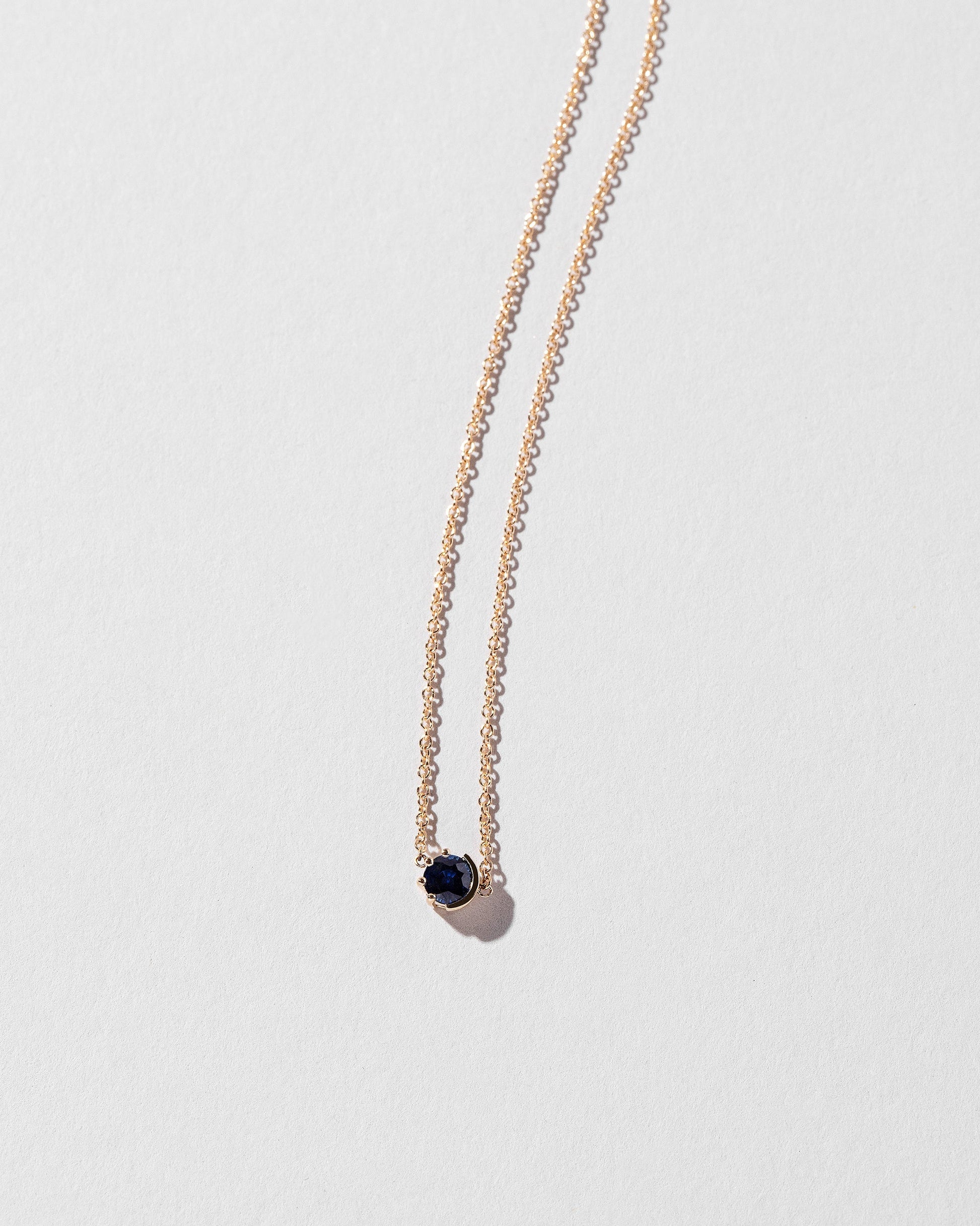 Closeup view of the Sapphire Sun & Moon Necklace on light color background.