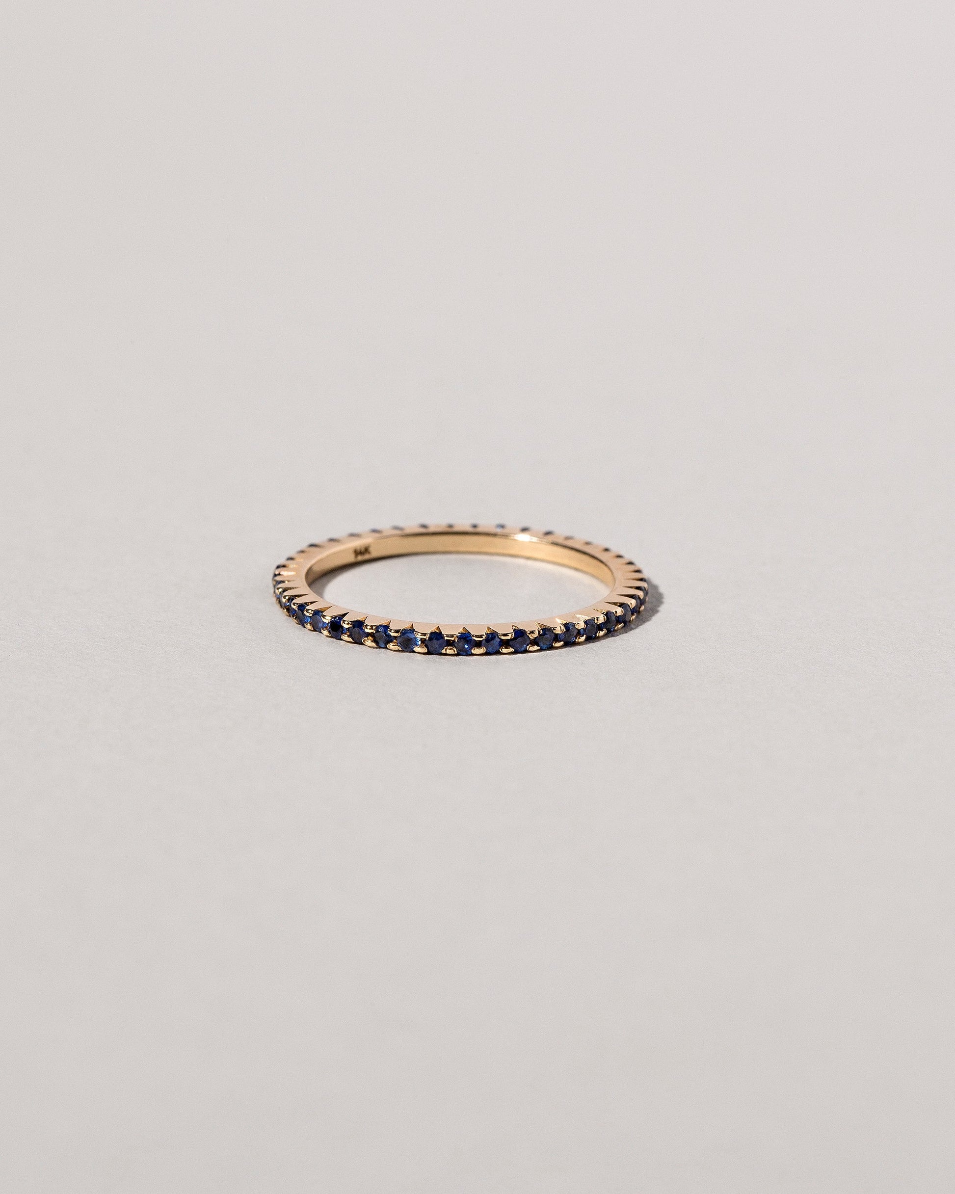 Closeup details of the Gold Blue Sapphire Gear Edge Band on light color background.