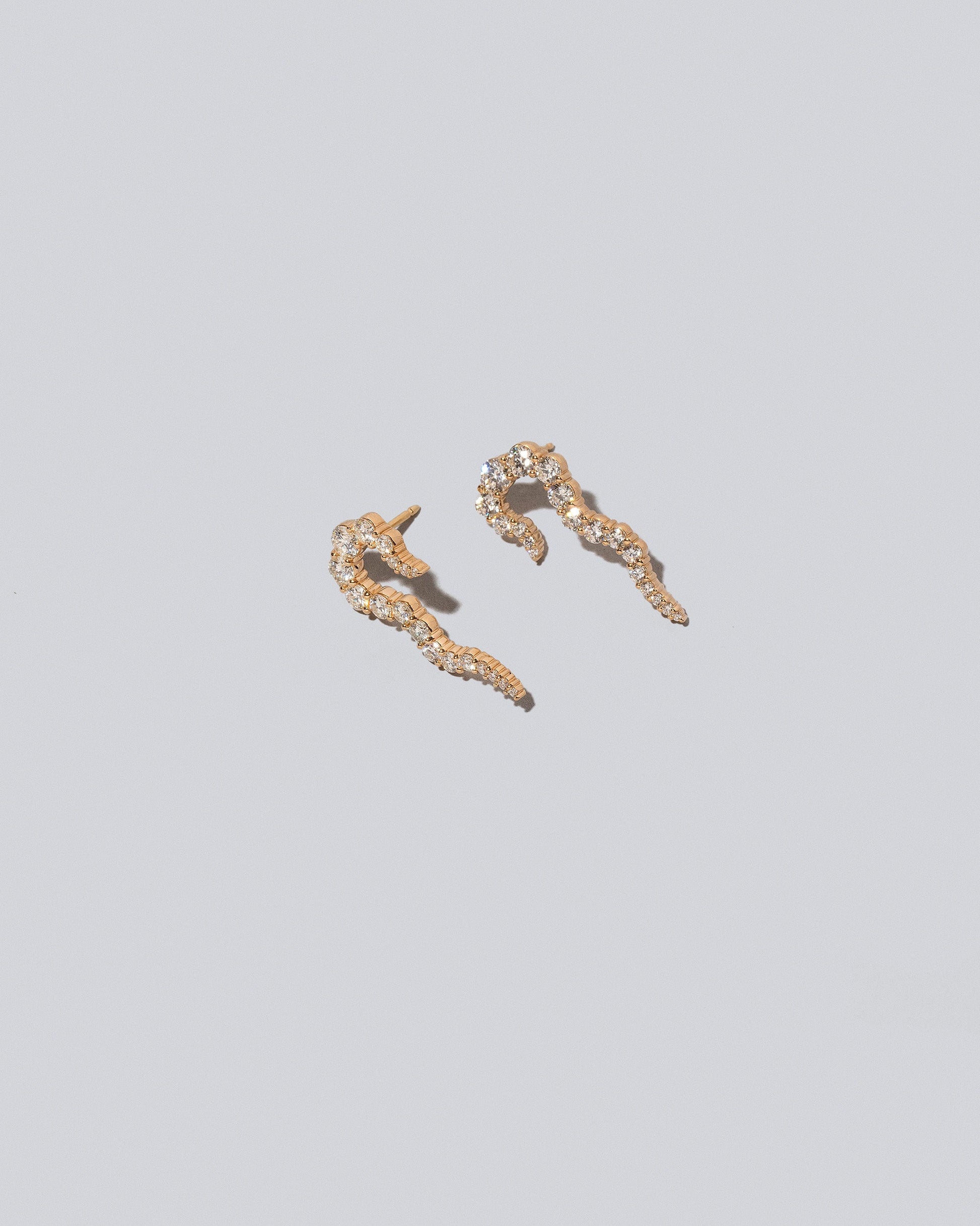 Closeup details of the Gold White Diamond Right Tidal Wave Earring Single and Gold White Diamond Left Tidal Wave Earring Single on light color background.