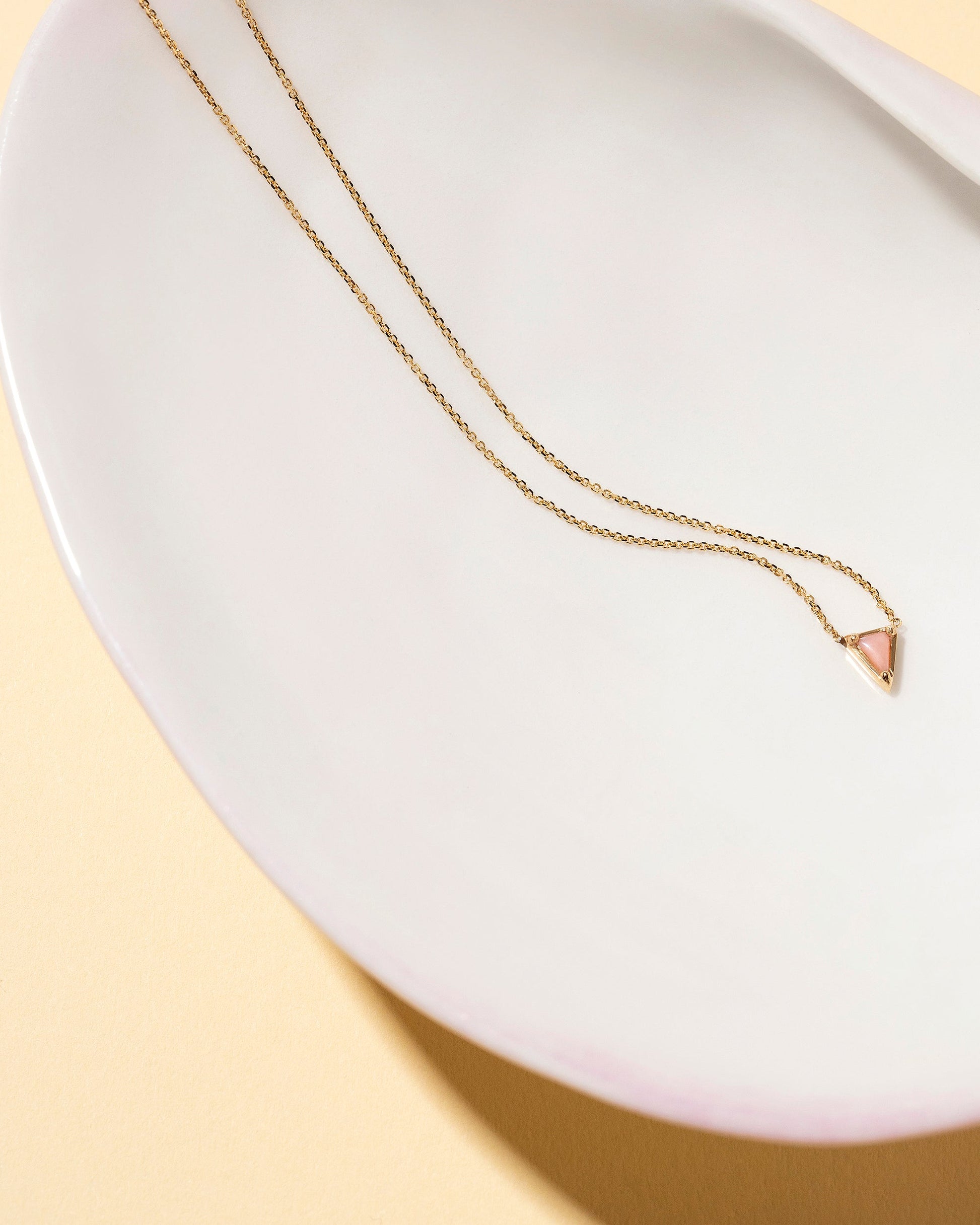 Gold Pink Opal Triangle Necklace on light color background.