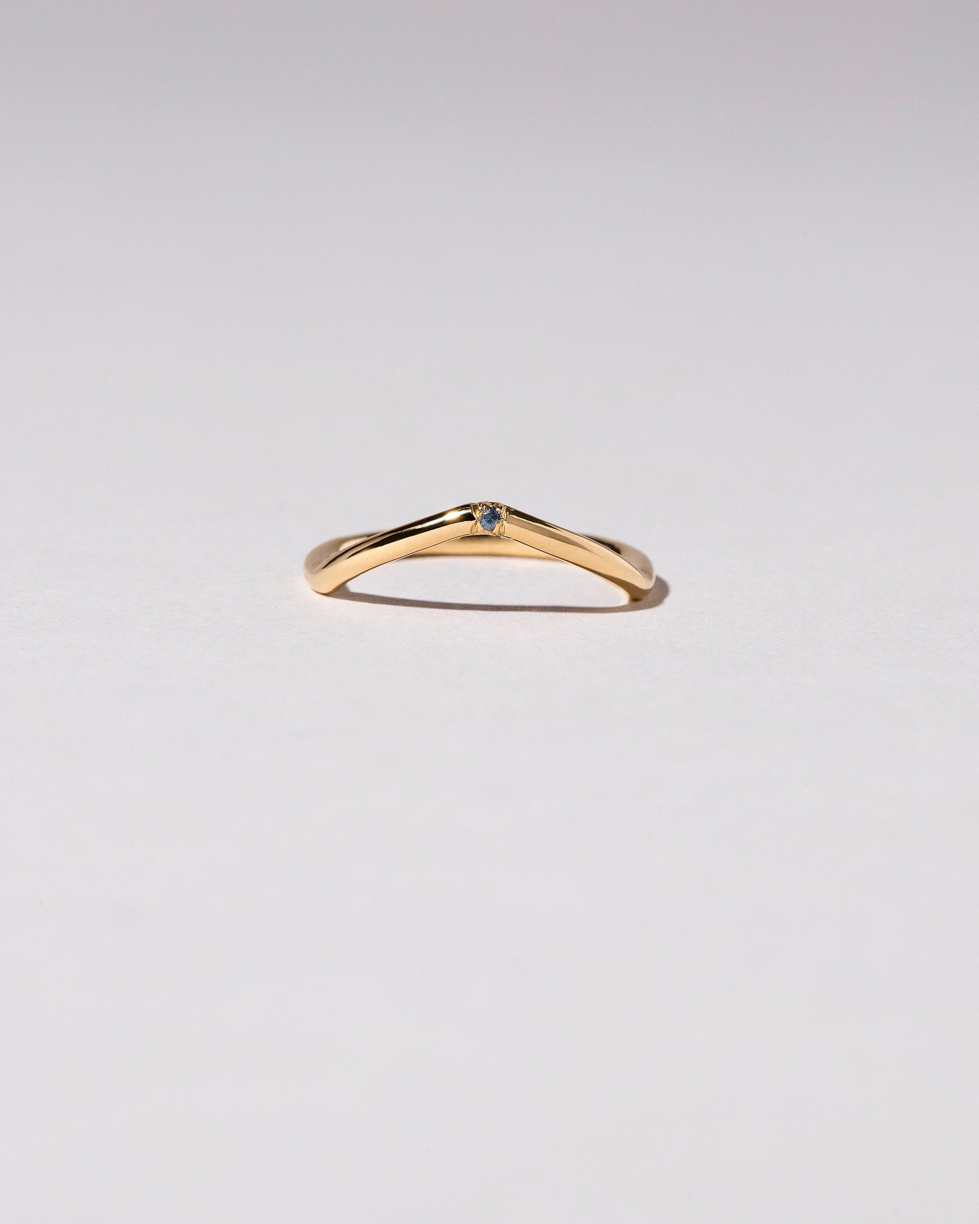 Gold Single Stone Blue Sapphire Low Peak Band on light color background.
