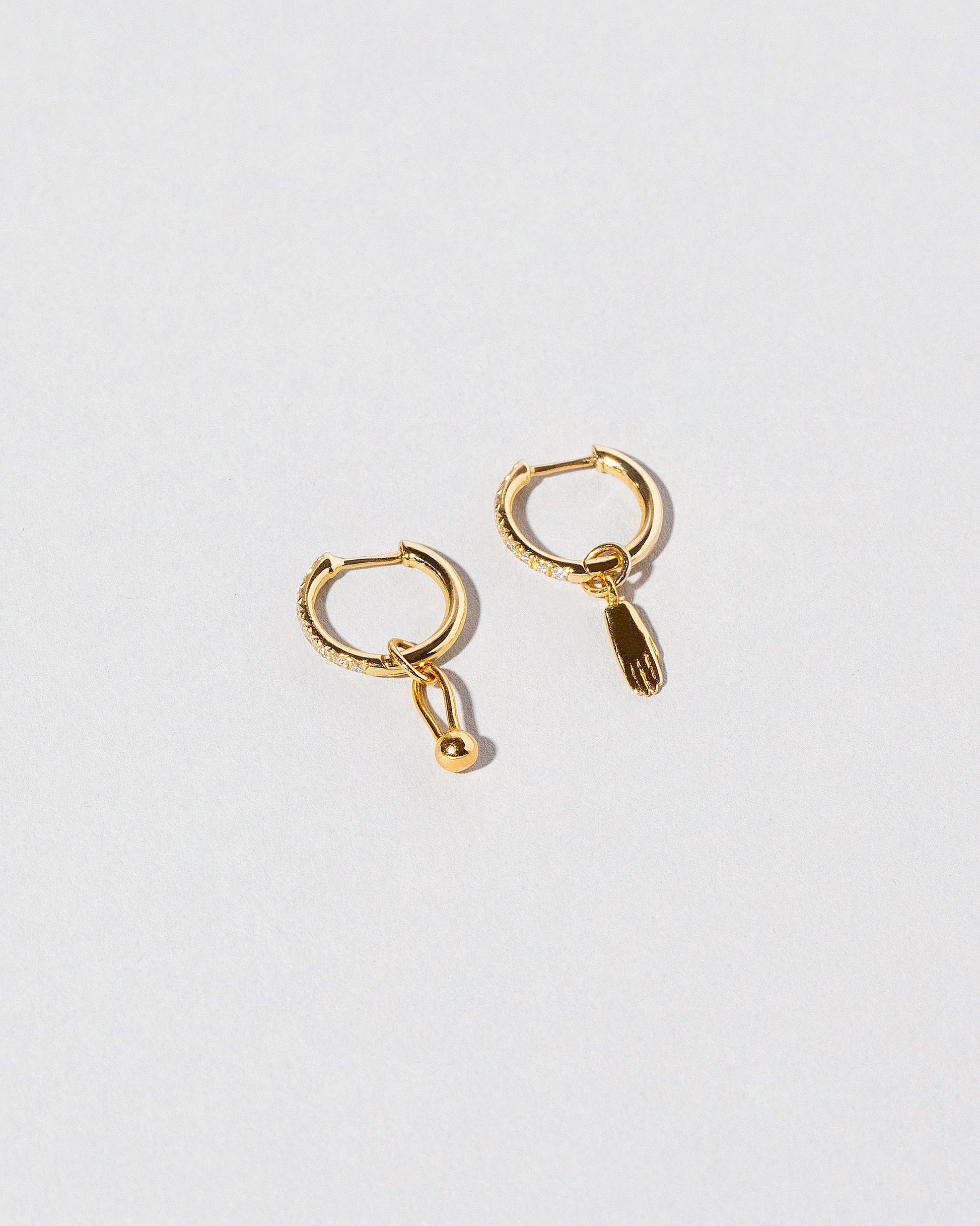 Gold Classic Diamond Snack Hoop Earrings with the Hand Talisman Charm and Loop & Sphere Talisman Charm on light color background.